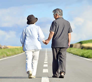 帽子を被った女性と男性が手を繋いで道路を歩く画像