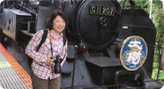 画像：機関車の前でカメラを持った鈴木さん